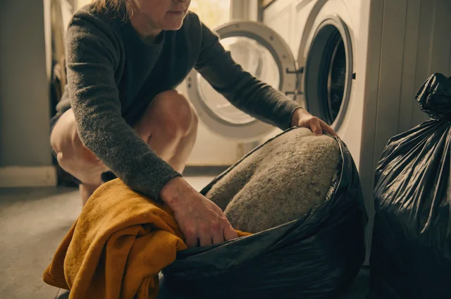 Homeowner bagging a dog bed at the source beside the washing machine, the first step in flea treatment for pet bedding with a hot wash at 60 degrees