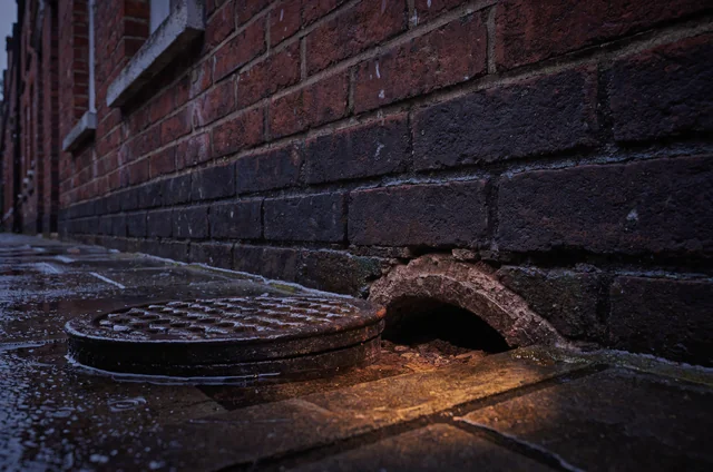 Exterior view of a cracked Victorian gully drain and eroded foundation brickwork after heavy rain, illustrating drainage vulnerabilities tied to the rodent infestation rise in England.