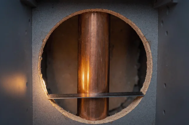 Close-up inspection measuring a mouse control kitchen cupboard gap size around a copper pipe entry with a metal rule.